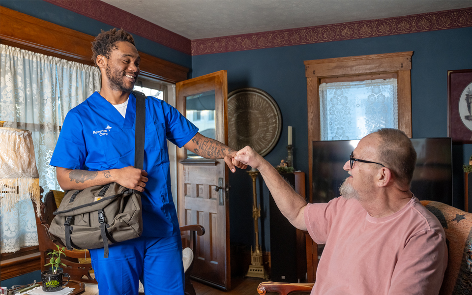 Man with bag, fist bumping man setting in chair. 
