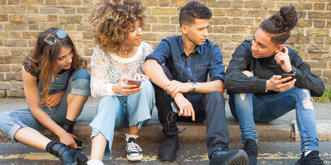 Group of teenagers sitting on a curb talking and using phones