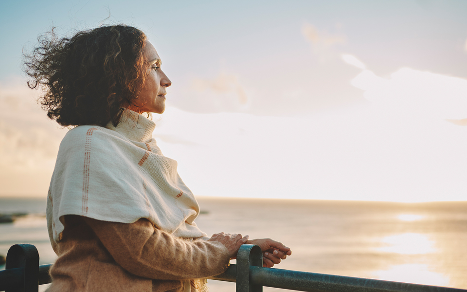 Woman wrapped in a shawl looking out over the ocean at sunset