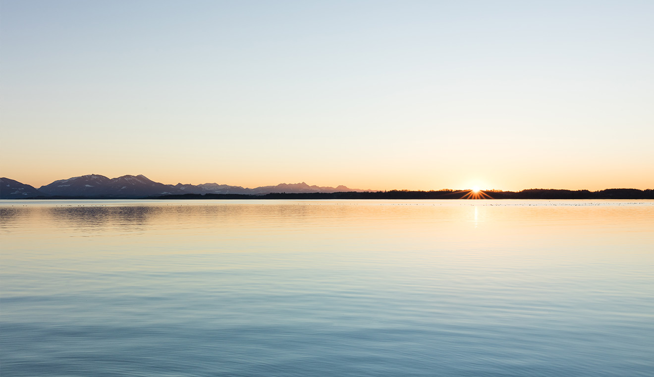Calm lake at sunrise with distant mountain silhouettes and still water