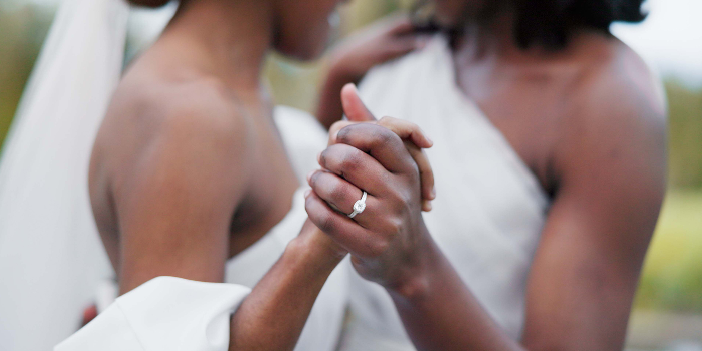 Close-up of two brides holding hands with engagement ring visible