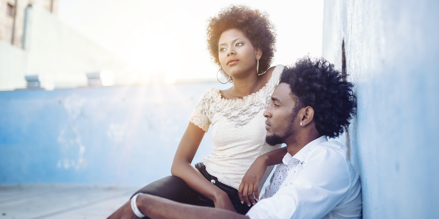 Young couple sitting together outdoors against a blue wall