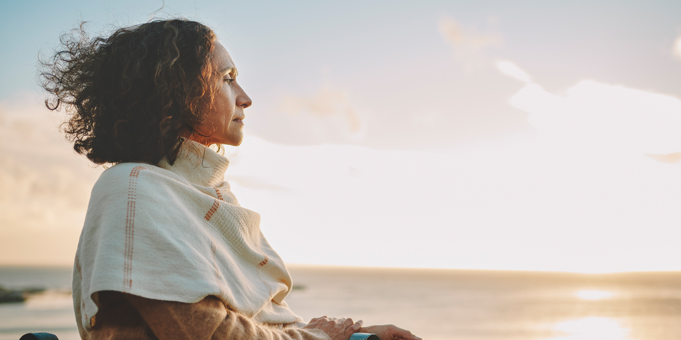Woman wrapped in a shawl looking out over the ocean at sunset