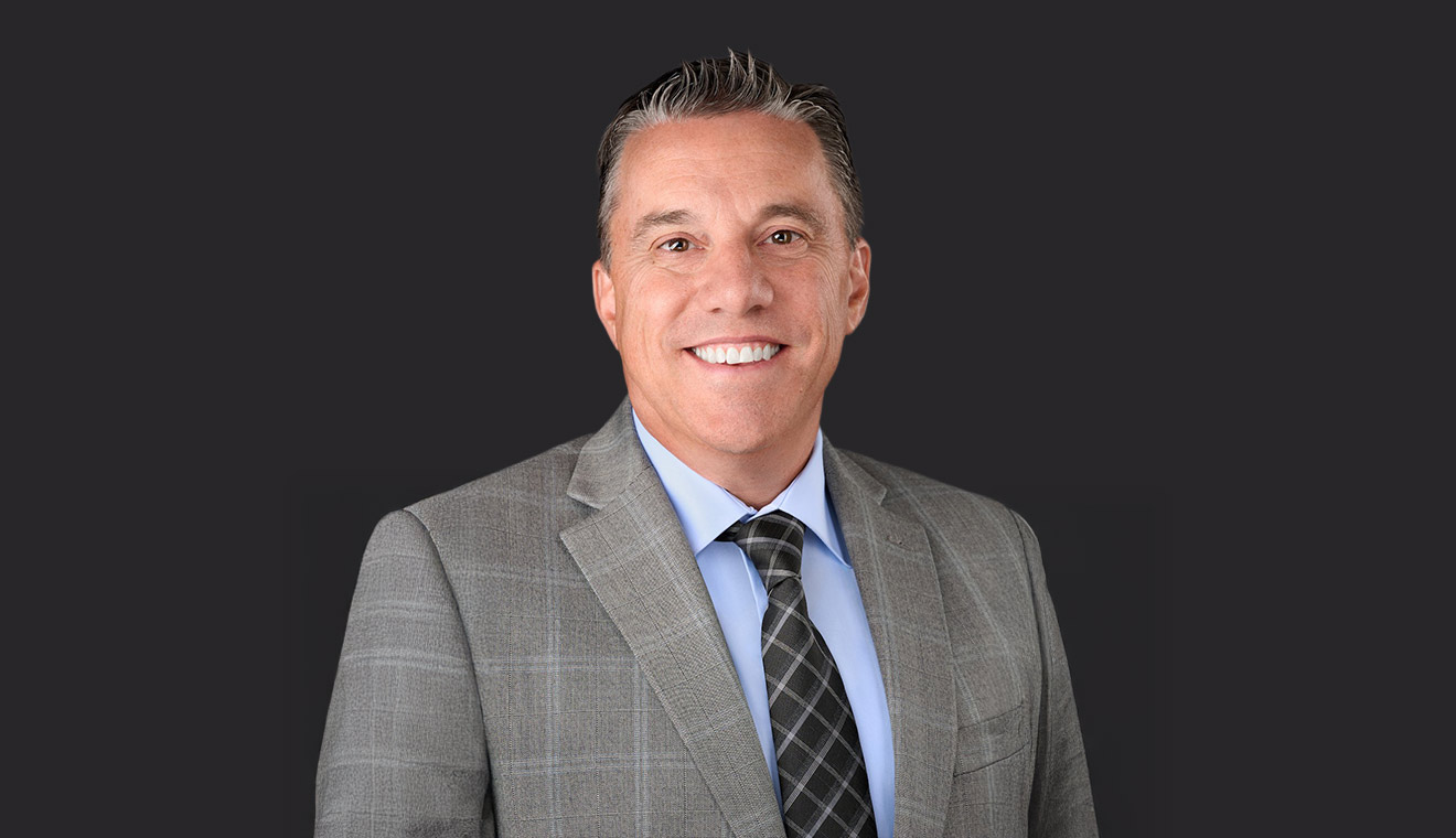Business executive in a gray plaid suit and black tie posing for a corporate headshot