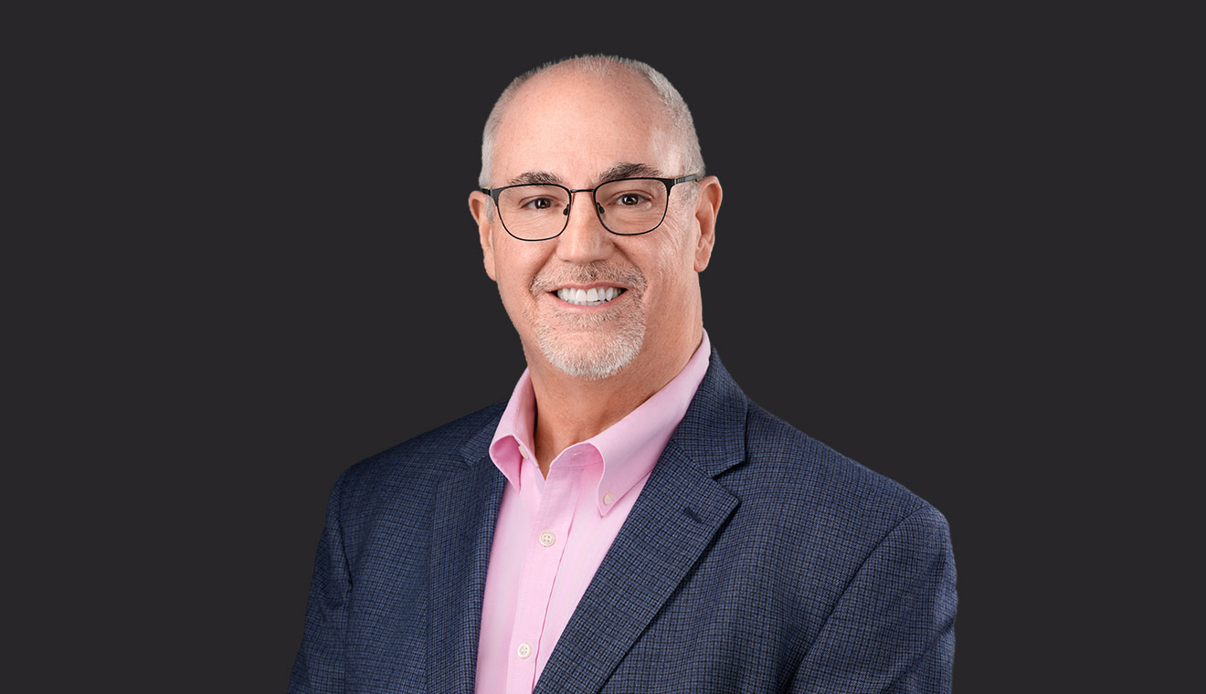 Man with glasses in a blue blazer and pink shirt smiling in a corporate headshot