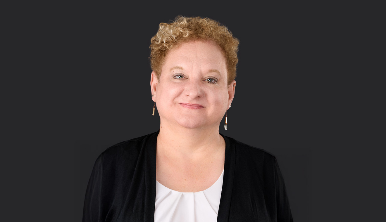 Curly-haired woman in black and white attire posing for a formal business portrait